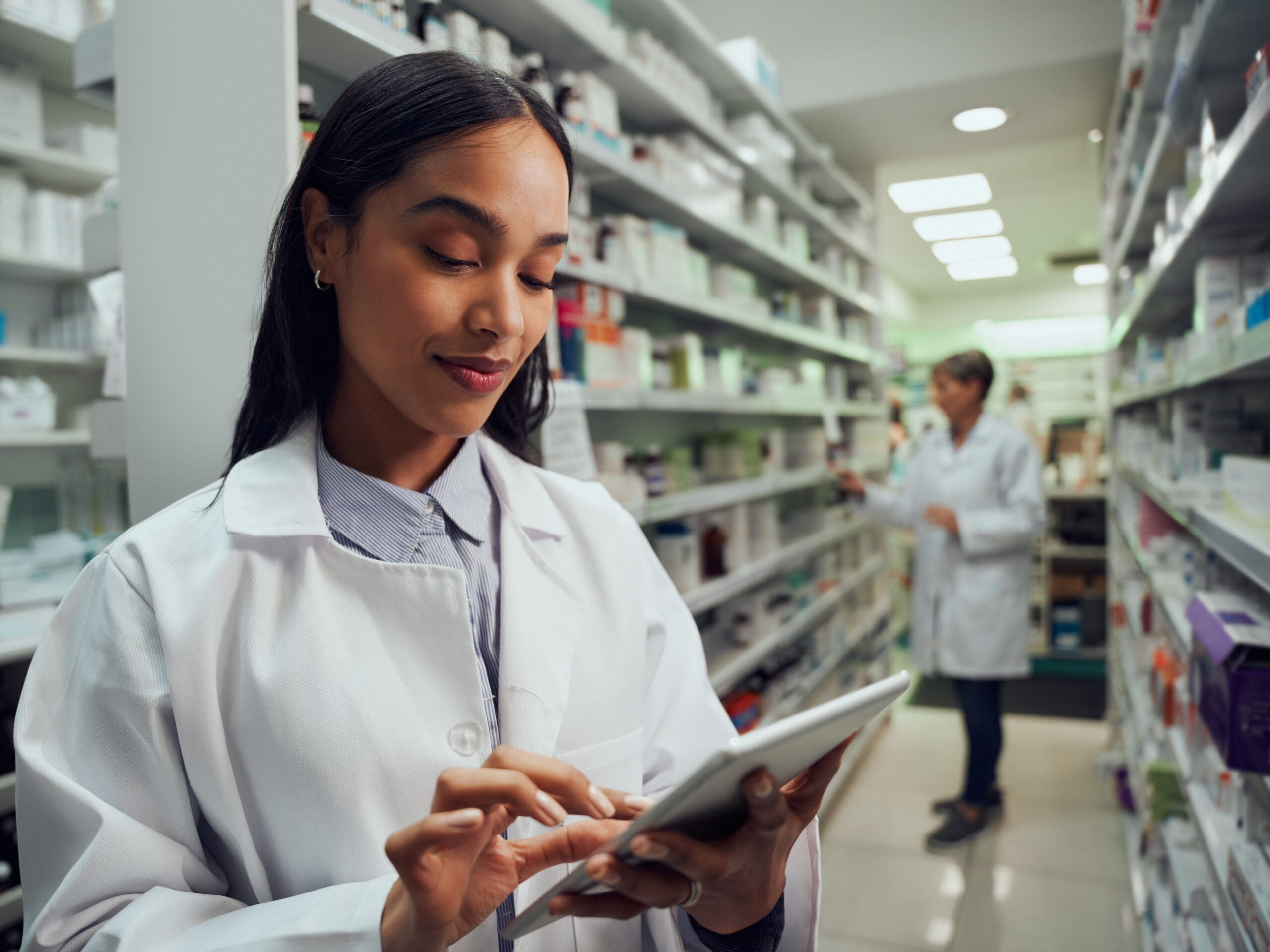 Female pharmacist looking at tablet with the pharmacy in the background.