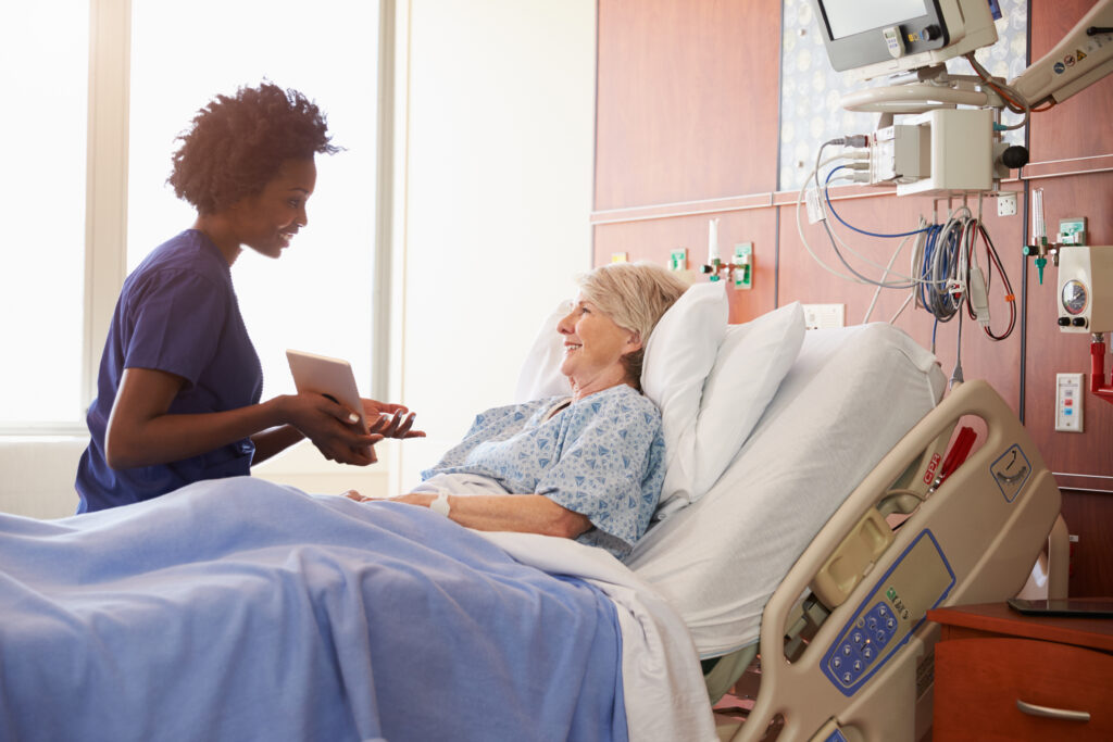 Pharmacy tech showing tablet to elderly patient at bedside