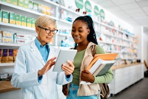 Older pharmacist holding tablet helping younger patient